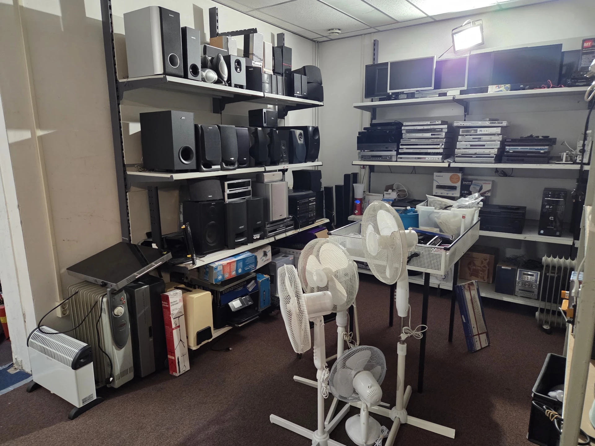 Stellingen met elektronische apparaten, speakers en ventilators in een kringloopwinkel