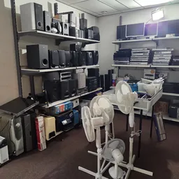 Stellingen met elektronische apparaten, speakers en ventilators in een kringloopwinkel