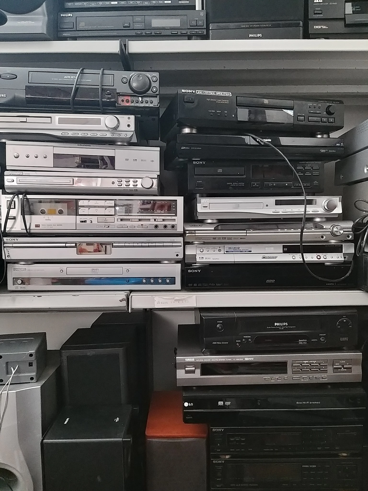 Verzameling vintage audio- en videoapparatuur gestapeld op elkaar, waaronder receivers, dvd-spelers en versterkers