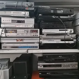 Verzameling vintage audio- en videoapparatuur gestapeld op elkaar, waaronder receivers, dvd-spelers en versterkers