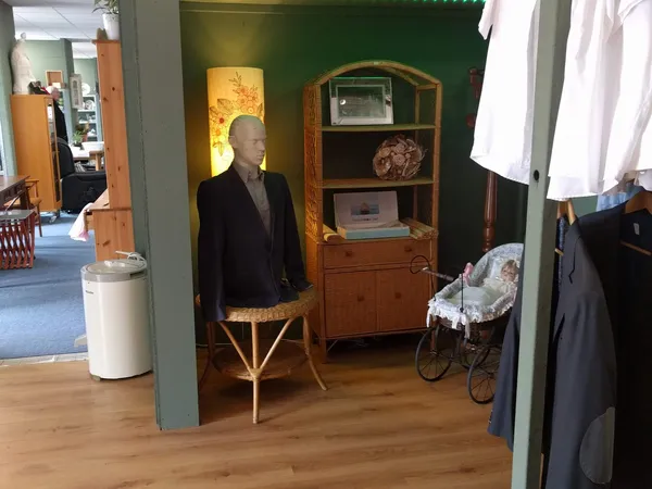 Winkelinterieur met houten meubels, etalagepop in blazer, kinderwagen en diverse spullen tegen groene muur