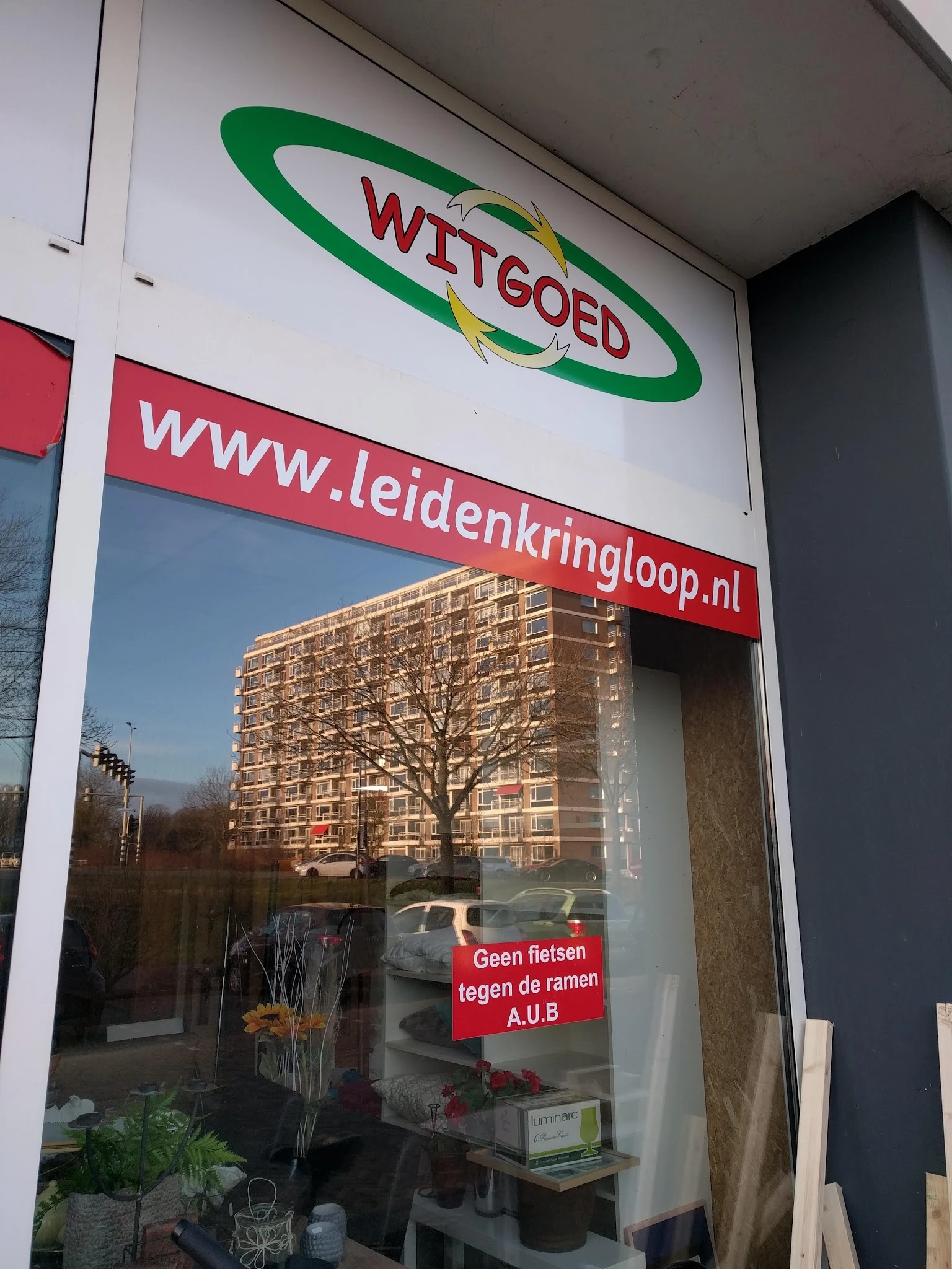 Winkelruit met website-adres www.leidenkringloop.nl, spiegeling van appartementengebouw en boom zichtbaar