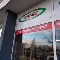Winkelruit met VINTAGE logo en rode banner '7 dagen p/w geopend', winkelstraat zichtbaar in reflectie