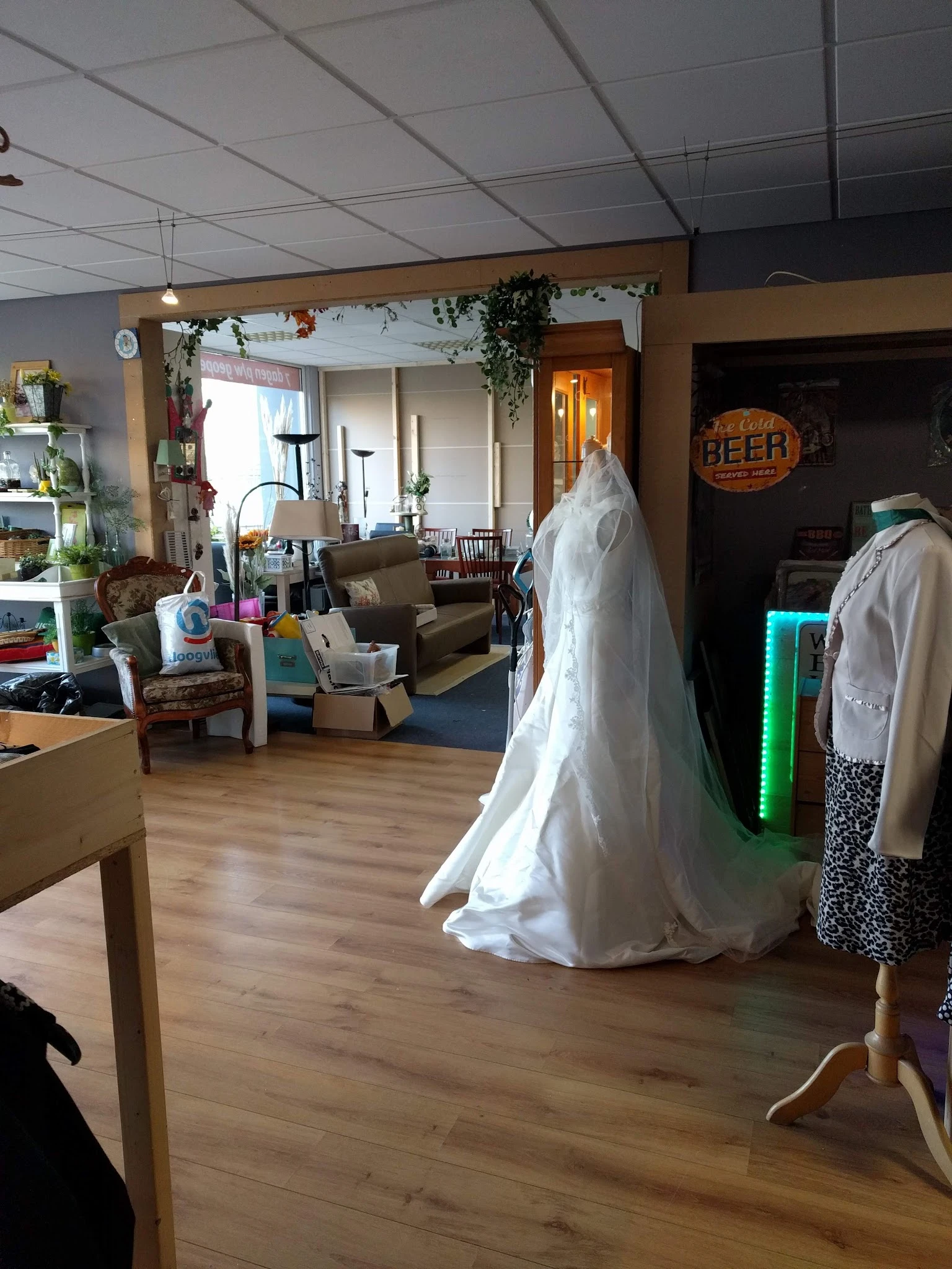 Interieur van kringloopwinkel met bruidsjurken op rekken en diverse meubels en spullen