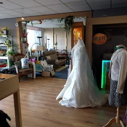 Interieur van kringloopwinkel met bruidsjurken op rekken en diverse meubels en spullen