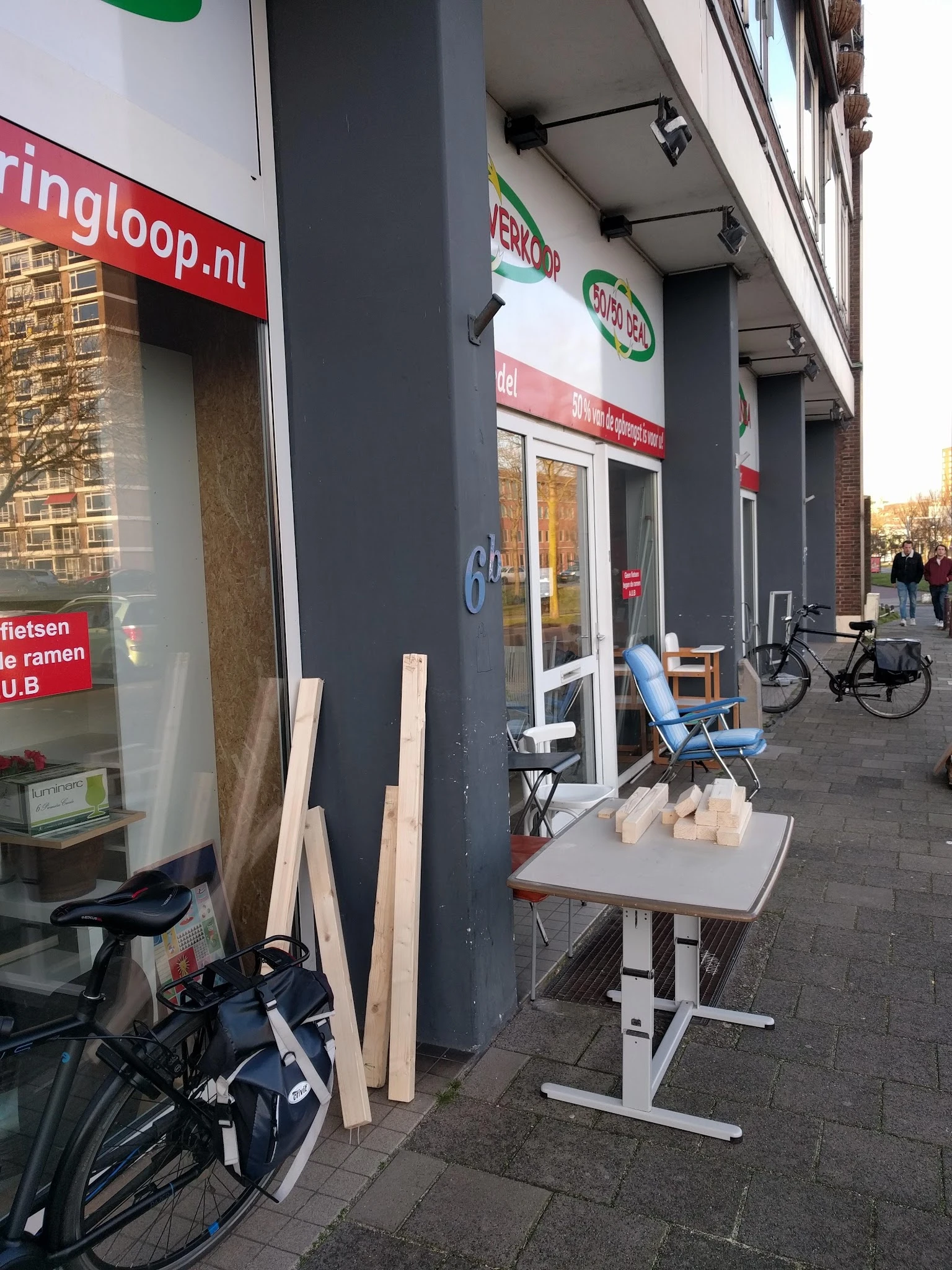 Winkelfront met donkere gevel, houten planken en blauwe stoelen op het terras, fiets ernaast