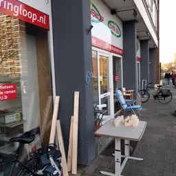 Winkelfront met donkere gevel, houten planken en blauwe stoelen op het terras, fiets ernaast