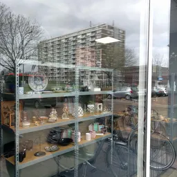 Metalen stellingkast achter glas met diverse tweedehands spullen zoals servies, decoratie en huishoudartikelen