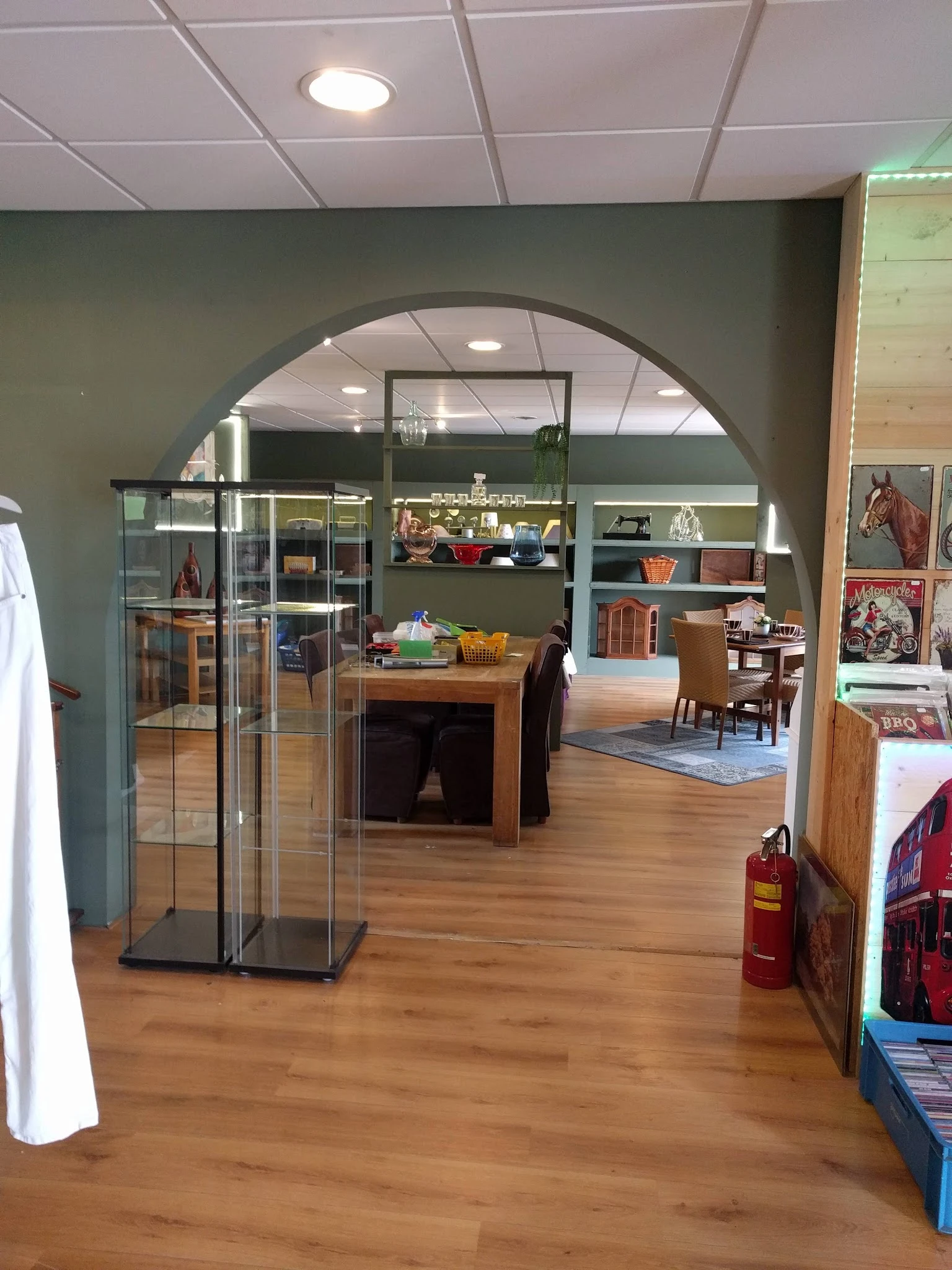Ruim winkelinterieur met houten vloer, glazen vitrines, houten meubels en groene wanden met rekken vol spullen
