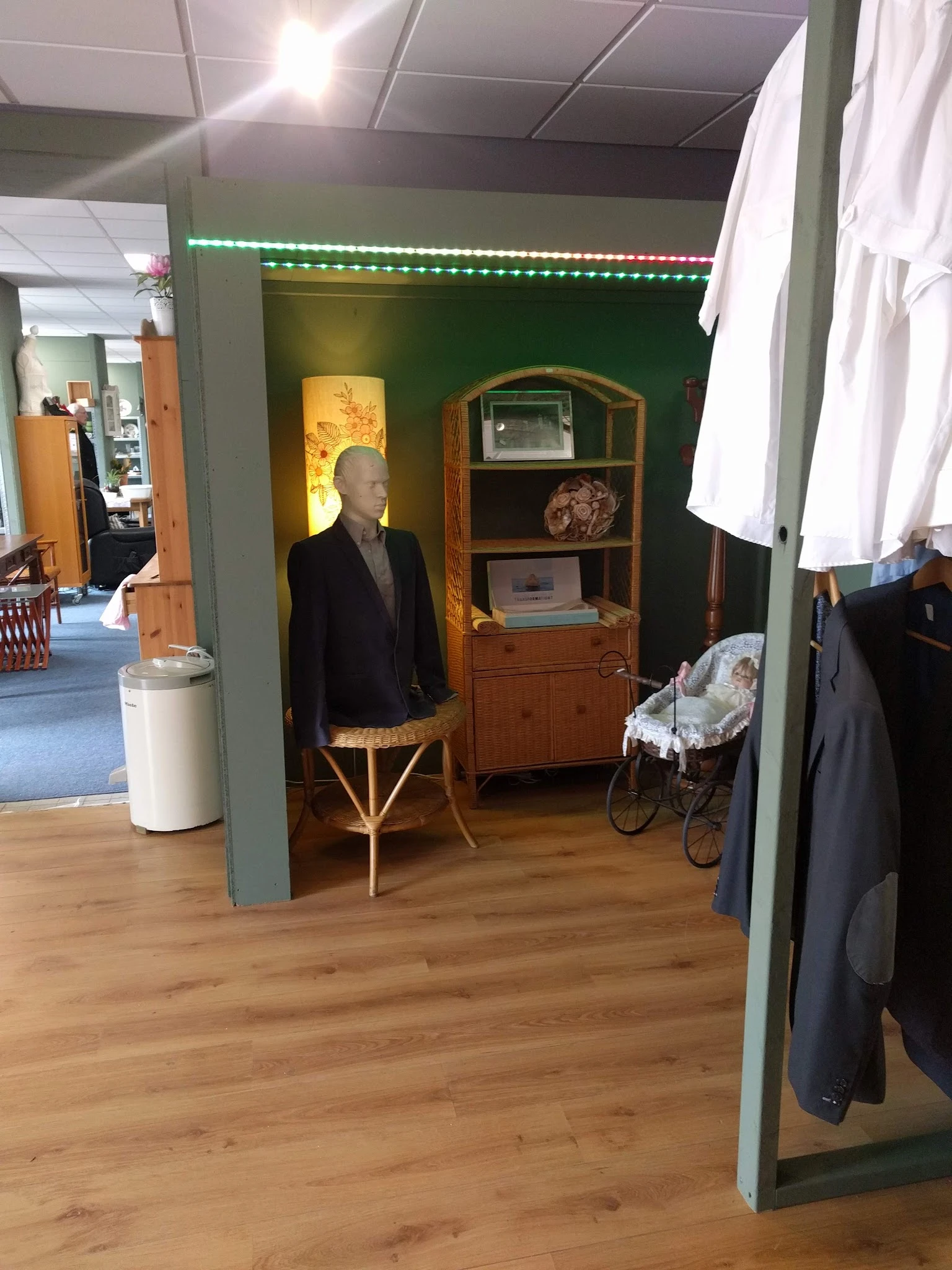 Winkelinterieur met houten meubels, etalagepop in zwart jasje, vintage kast en kinderwagen tegen groene muur