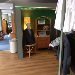 Winkelinterieur met houten meubels, etalagepop in zwart jasje, vintage kast en kinderwagen tegen groene muur