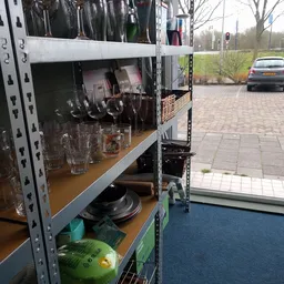 Stellingrek met glazen, borden en huishoudelijke artikelen in de kringloopwinkel