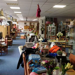 Brede blik op de winkelvloer met diverse tweedehands spullen, meubels, decoraties en stellingen langs de zijkanten.