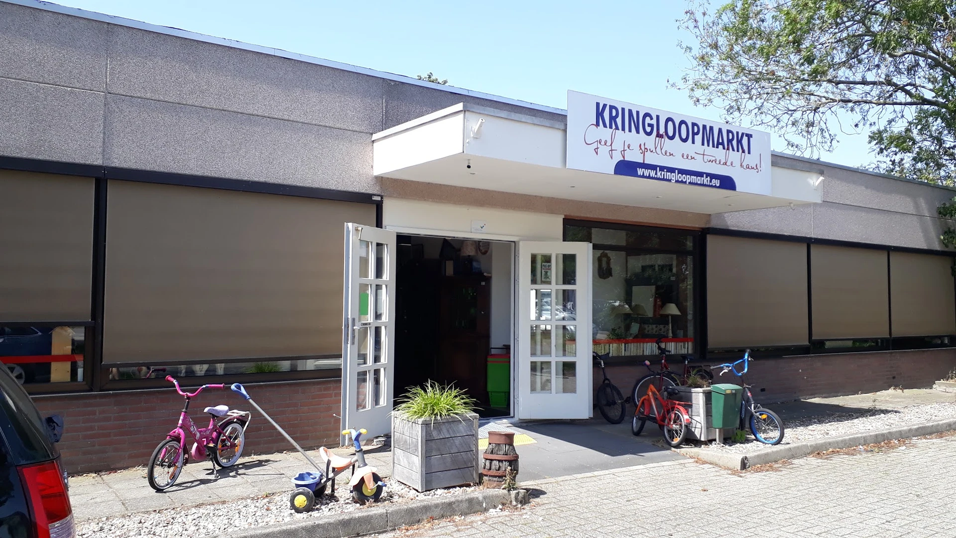 Winkelpui van Kringloopmarkt met witte deuren, naam op uithangbord, fietsen ervoor