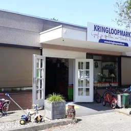 Winkelpui van Kringloopmarkt met witte deuren, naam op uithangbord, fietsen ervoor