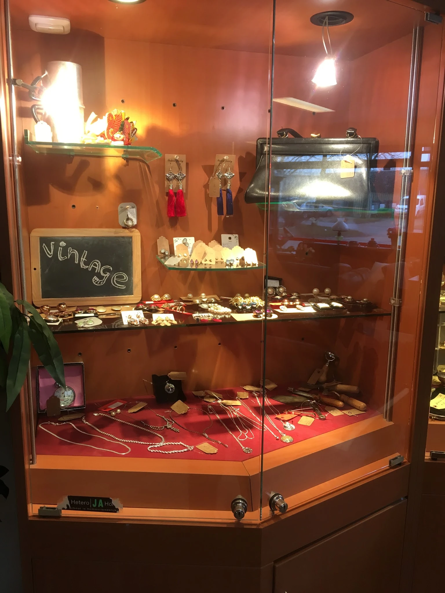 Glazen vitrine met uitgestalde vintage sieraden, kettingen, ringen en accessoires op rode achtergrond