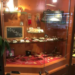 Glazen vitrine met uitgestalde vintage sieraden, kettingen, ringen en accessoires op rode achtergrond