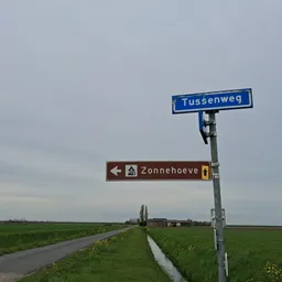 Straatnaamborden Tussenweg en Zonnehoeve langs een landelijke weg met groene velden