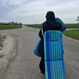 Persoon van achteren met kitesurfboard op een landweggetje tussen groene velden