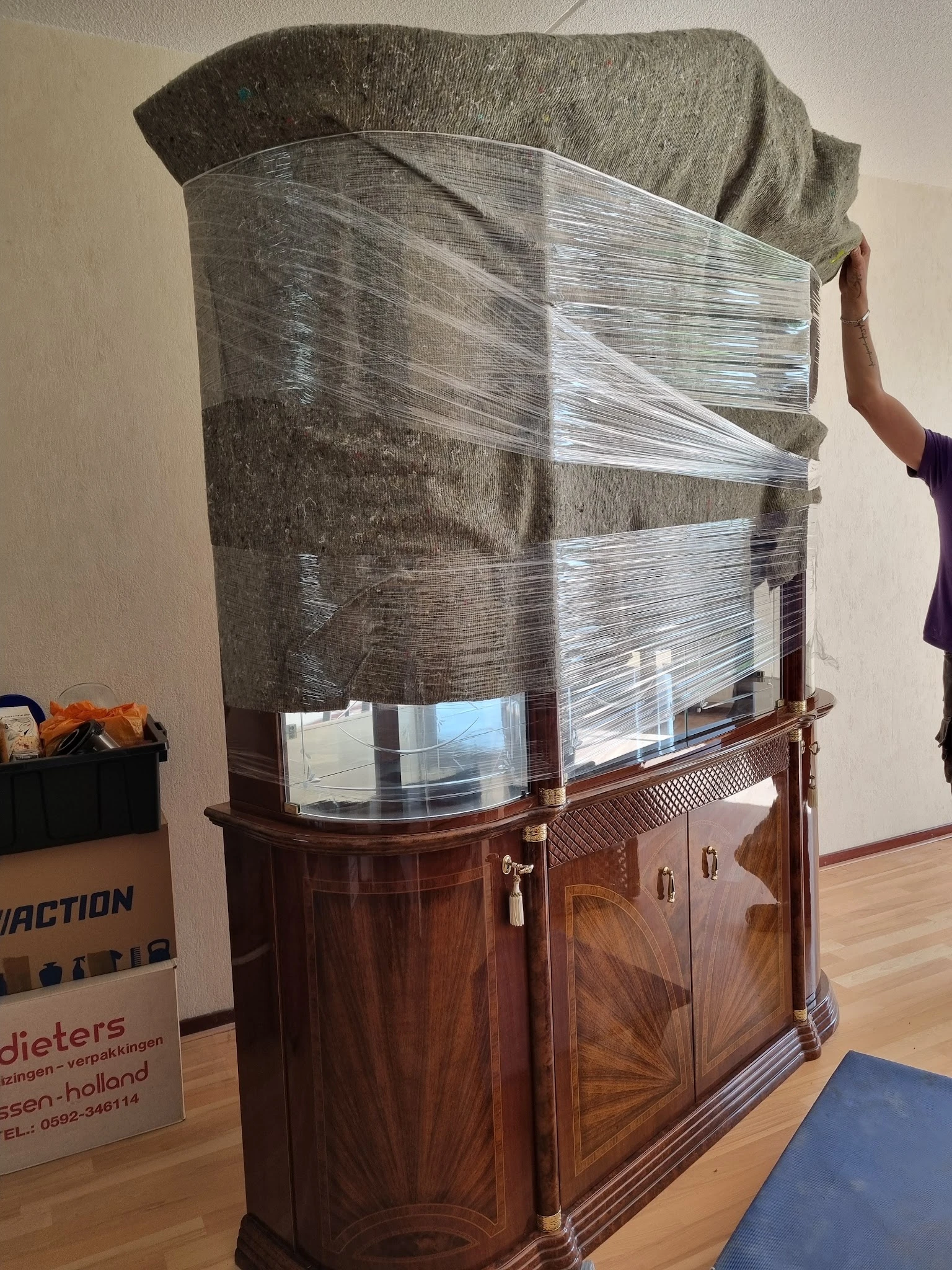 Houten vitrinekast met glazen deuren, gedeeltelijk ingepakt in plastic wrap