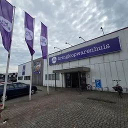 Voorkant van kringloopwarenhuis met paarse vlaggen en duidelijk zichtbare winkelnaambord