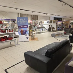 Winkelinterieur met zwarte bank op voorgrond, displays met huishoudartikelen en een blauwe promotiebanner op de achtergrond