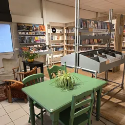 Winkelvloer met groene tafel, stoelen, planten en boekenkasten op de achtergrond