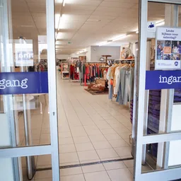 Binnenaanzicht van kringloopwinkel met kledingrekken en stellingen vol tweedehands artikelen