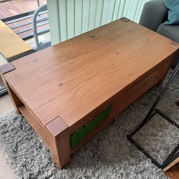 Houten salontafel met dikke blokpoten en groene laden, op grijze vloerkleed in de winkel