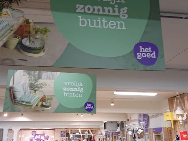 Winkelinterieur met groene promotionele banners aan het plafond met tekst 'vrolijk zonnig buiten' en het logo 'het goed'