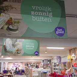 Winkelinterieur met groene promotionele banners aan het plafond met tekst 'vrolijk zonnig buiten' en het logo 'het goed'