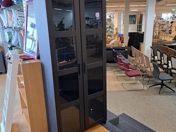 Winkelinterieur met zwarte vitrinekast, houten display links, rode en zwarte stoelen, en zicht op verdere winkelvloer met ste