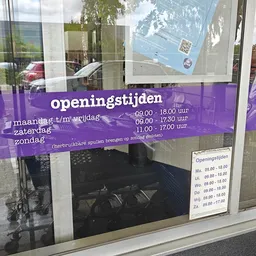 Paarse banner met openingstijden van een winkel op glaswand