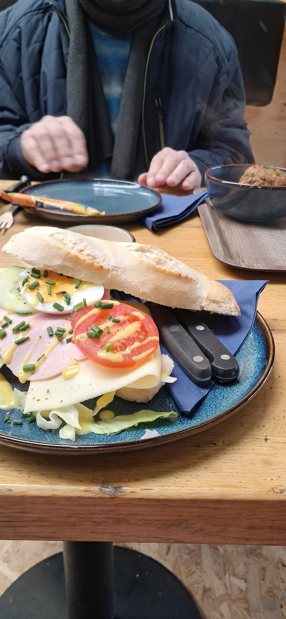 Broodje met kaas, ham, tomaat en ui op blauwe bord met bestek