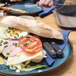 Broodje met kaas, ham, tomaat en ui op blauwe bord met bestek
