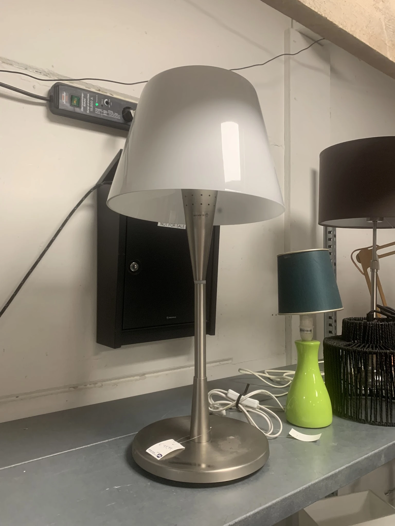 Staande lamp met witte kap en metalen poot naast groene vaas en andere lampen