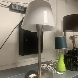 Staande lamp met witte kap en metalen poot naast groene vaas en andere lampen