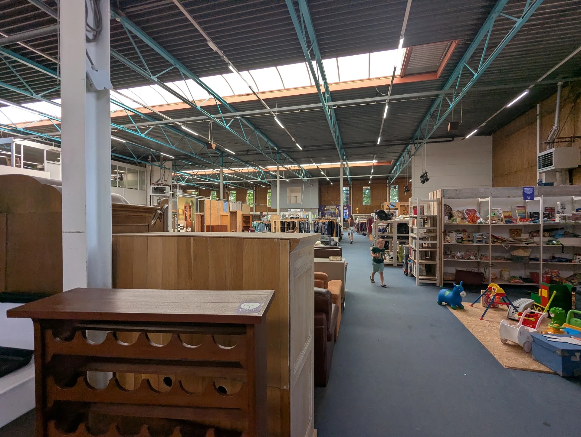 Winkelvloer van kringloopwinkel met houten meubels op voorgrond en stellingen met spullen in achtergrond