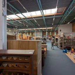 Winkelvloer van kringloopwinkel met houten meubels op voorgrond en stellingen met spullen in achtergrond