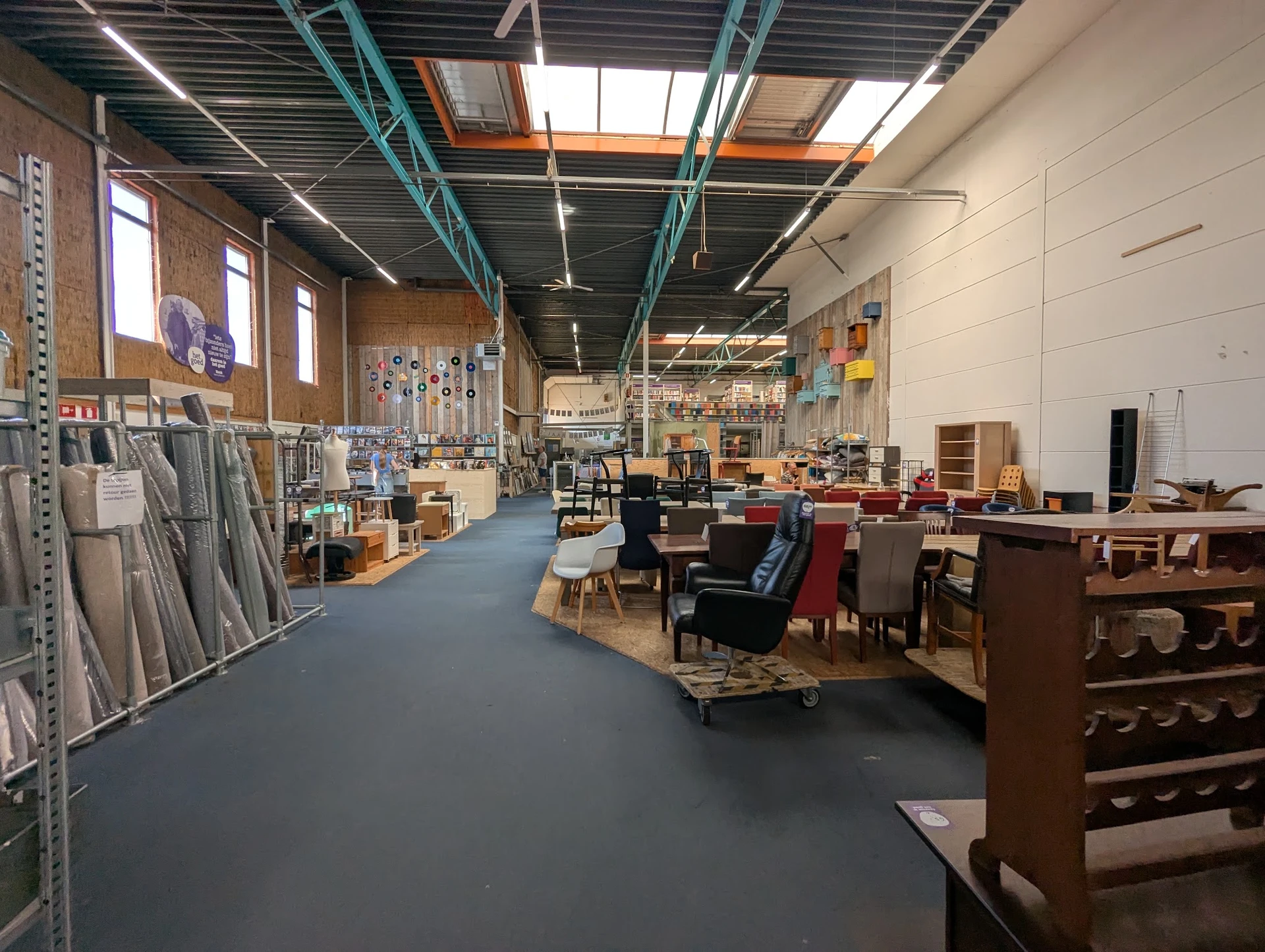 Ruim magazijn met houten meubels, stoelen en diverse spullen langs stellingen en op de vloer