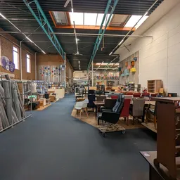 Ruim magazijn met houten meubels, stoelen en diverse spullen langs stellingen en op de vloer