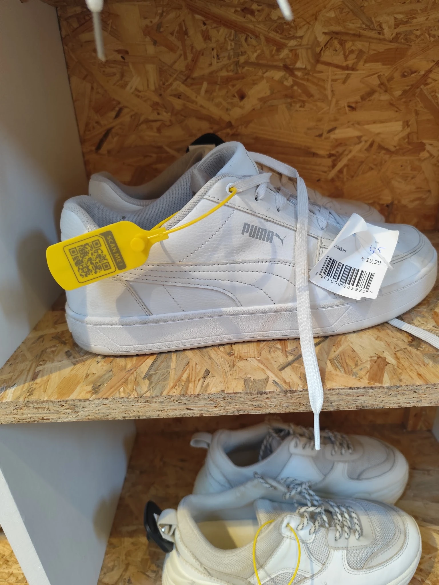 Witte Puma sneaker met gele kledingclip en verkoopkaartje op kurken ondergrond