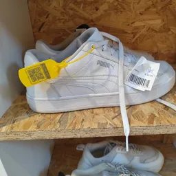 Witte Puma sneaker met gele kledingclip en verkoopkaartje op kurken ondergrond