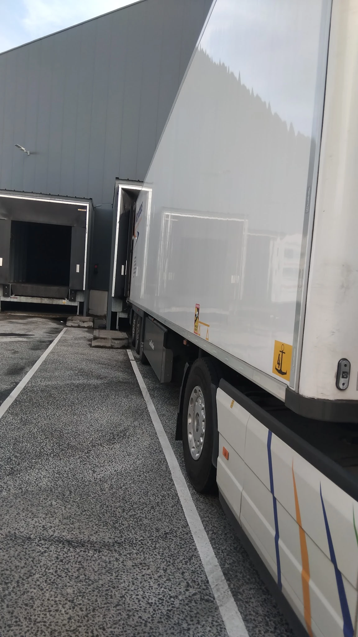 Bedrijfsbus met oplegger op parkeerterrein naast winkelgebouw