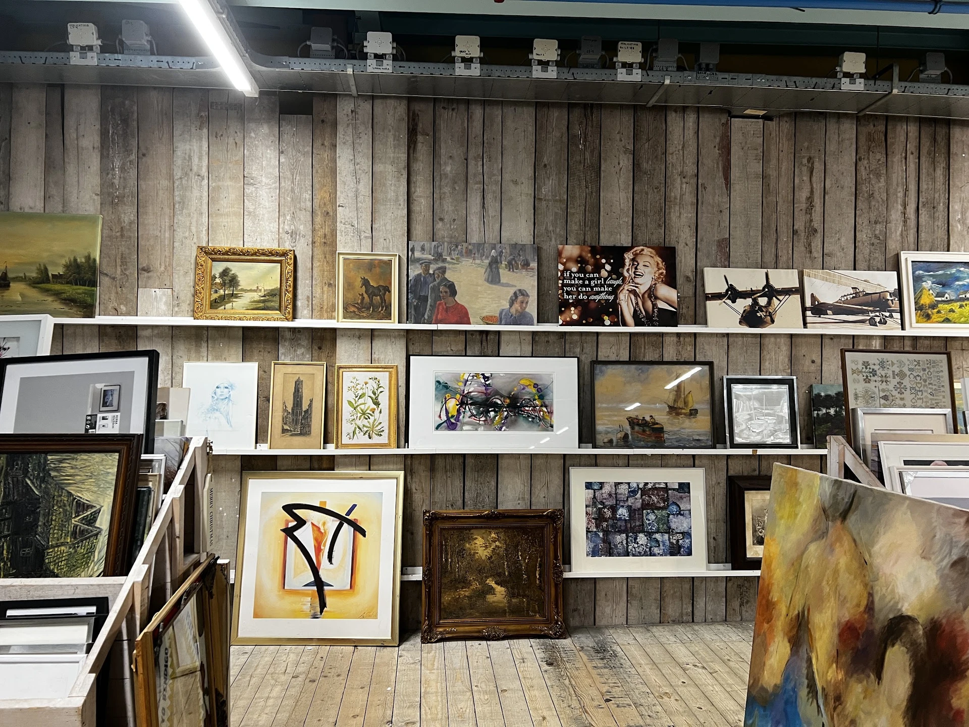 Houten wand met opgstelde schilderijen, prenten en kunstwerken in diverse formaten en stijlen