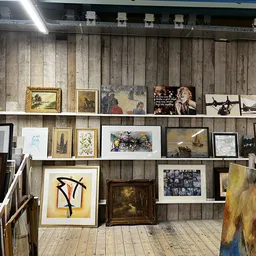 Houten wand met opgstelde schilderijen, prenten en kunstwerken in diverse formaten en stijlen