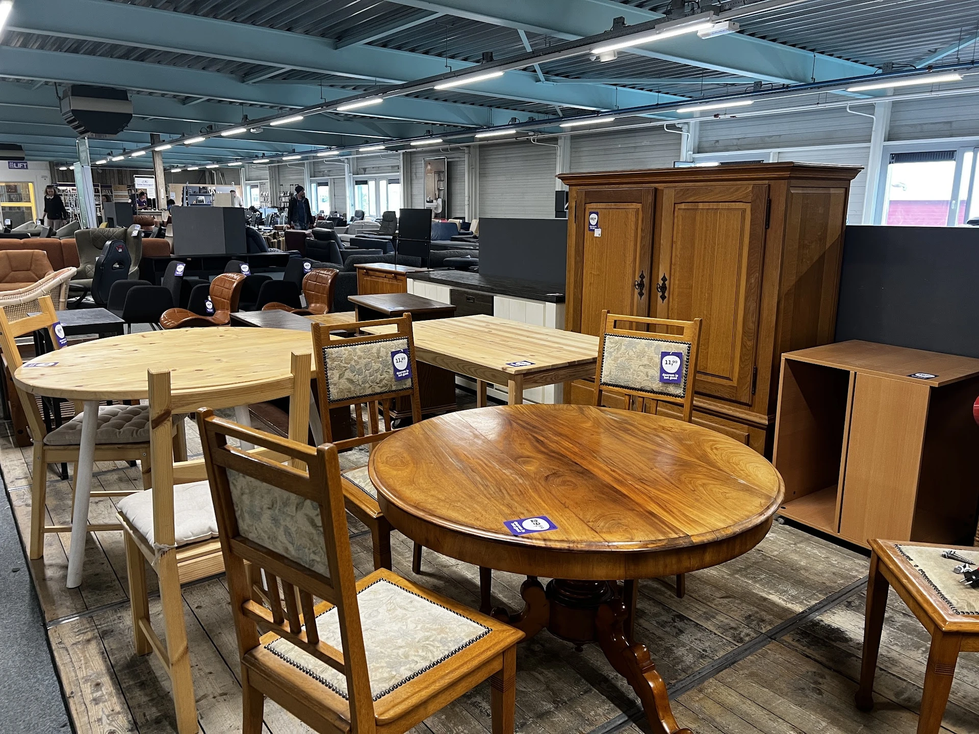 Uitgestalde meubels in de kringloopwinkel: houten tafels, stoelen en kasten
