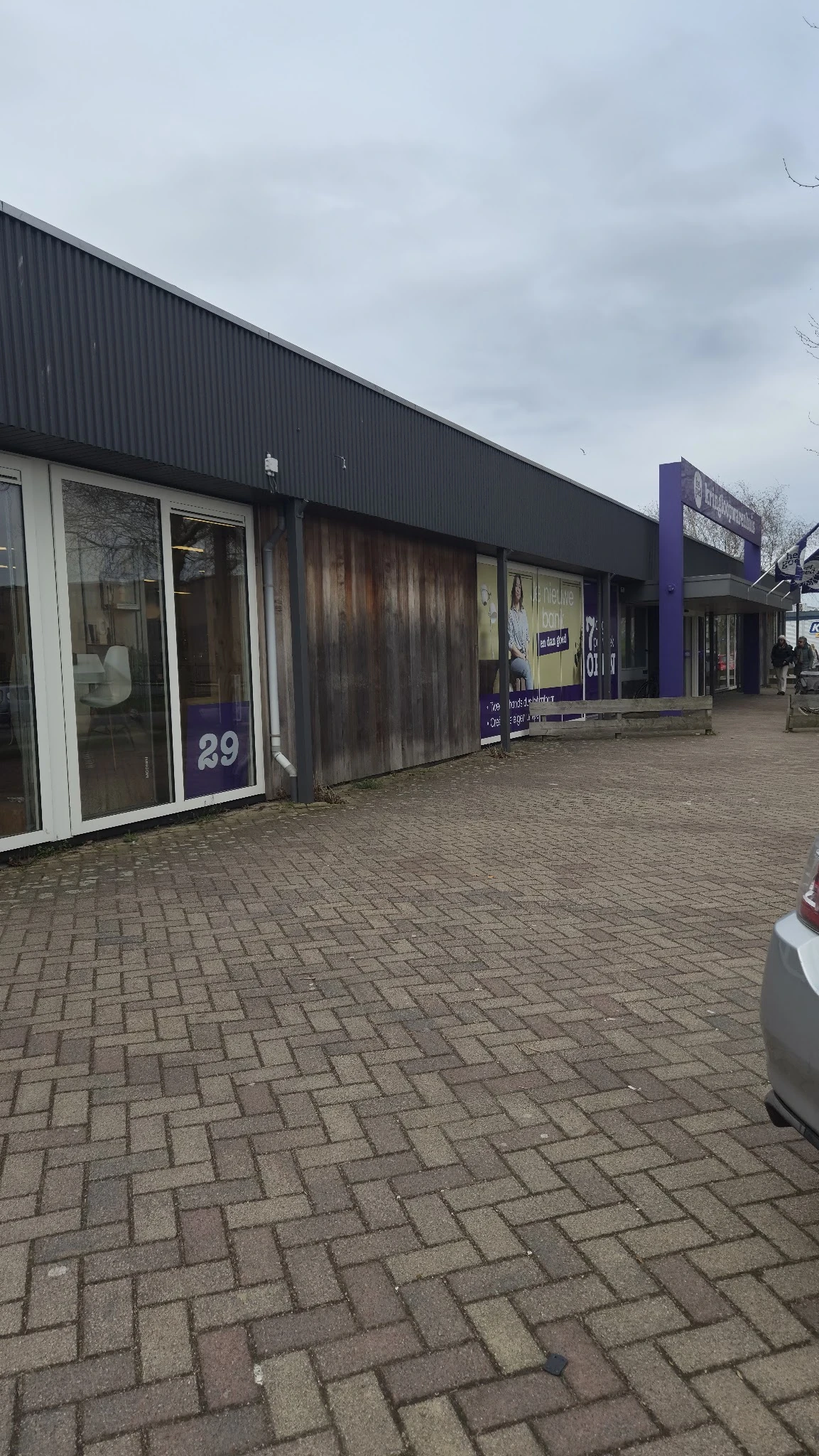 Voorgevel van kringloopwinkel met winkelruit nummer 29 en aangrenzen winkel, op bakstenen plein