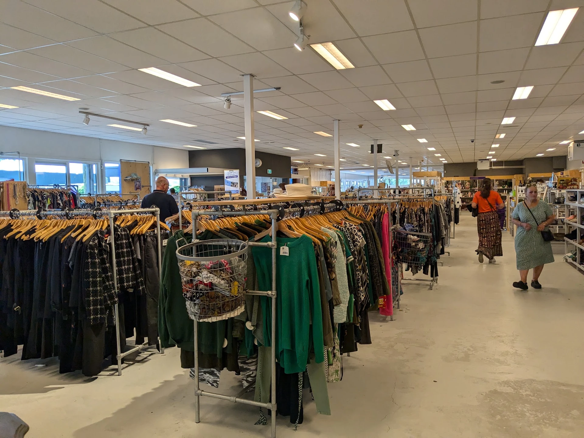 Rekken met tweedehands kleding op hangers in een grote winkelruimte met fluorescente verlichting
