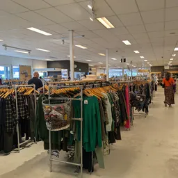 Rekken met tweedehands kleding op hangers in een grote winkelruimte met fluorescente verlichting